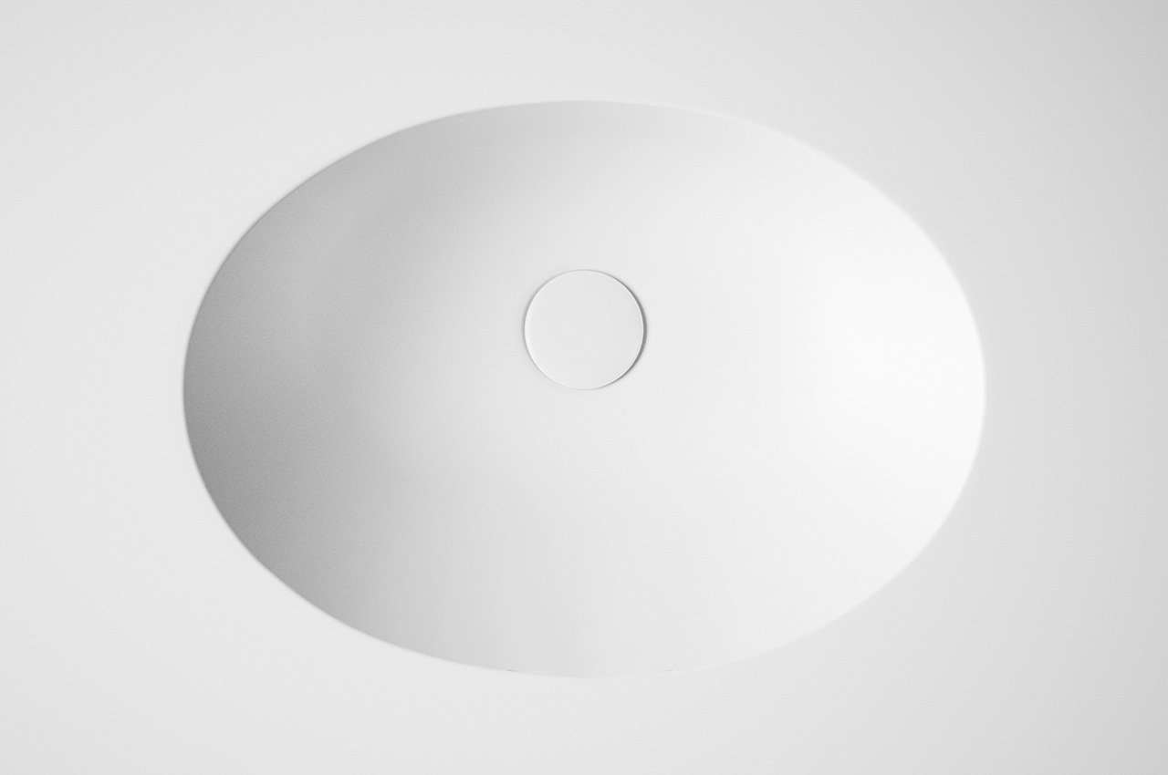 A minimalistic, top-down view of a round, white object with a smaller circular center, resembling a modern ceiling light fixture against a plain white background.