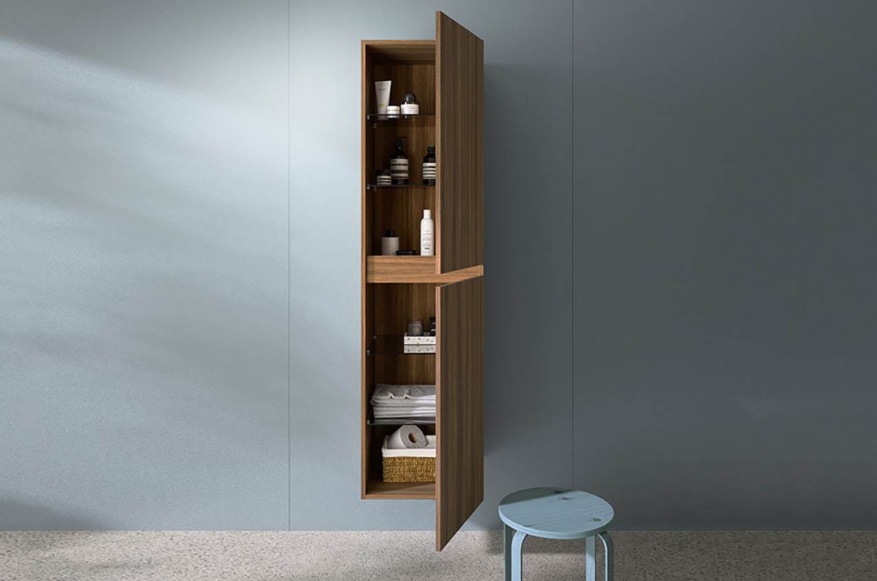 Ein hoher, schmaler Holzschrank mit offener Tür bietet Platz für Flaschen, Handtücher und einen Korb. Diese schlichte Aufbewahrungslösung ist an einer schlichten grauen Wand mit stilvollem Wandpaneele über einem hellblauen runden Hocker montiert.