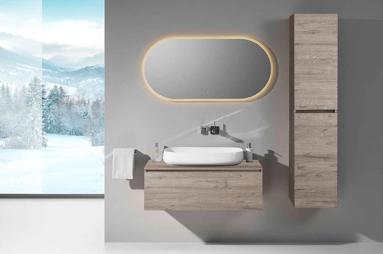 Minimalistisches Bad mit badmöbel holzoptik, Gefäßwaschbecken, Wandarmatur, Hochschrank, beleuchtetem ovalen Spiegel, Handtuch auf der linken Seite und einem großen Fenster, das eine verschneite Winterlandschaft mit Bäumen und Bergen zeigt.