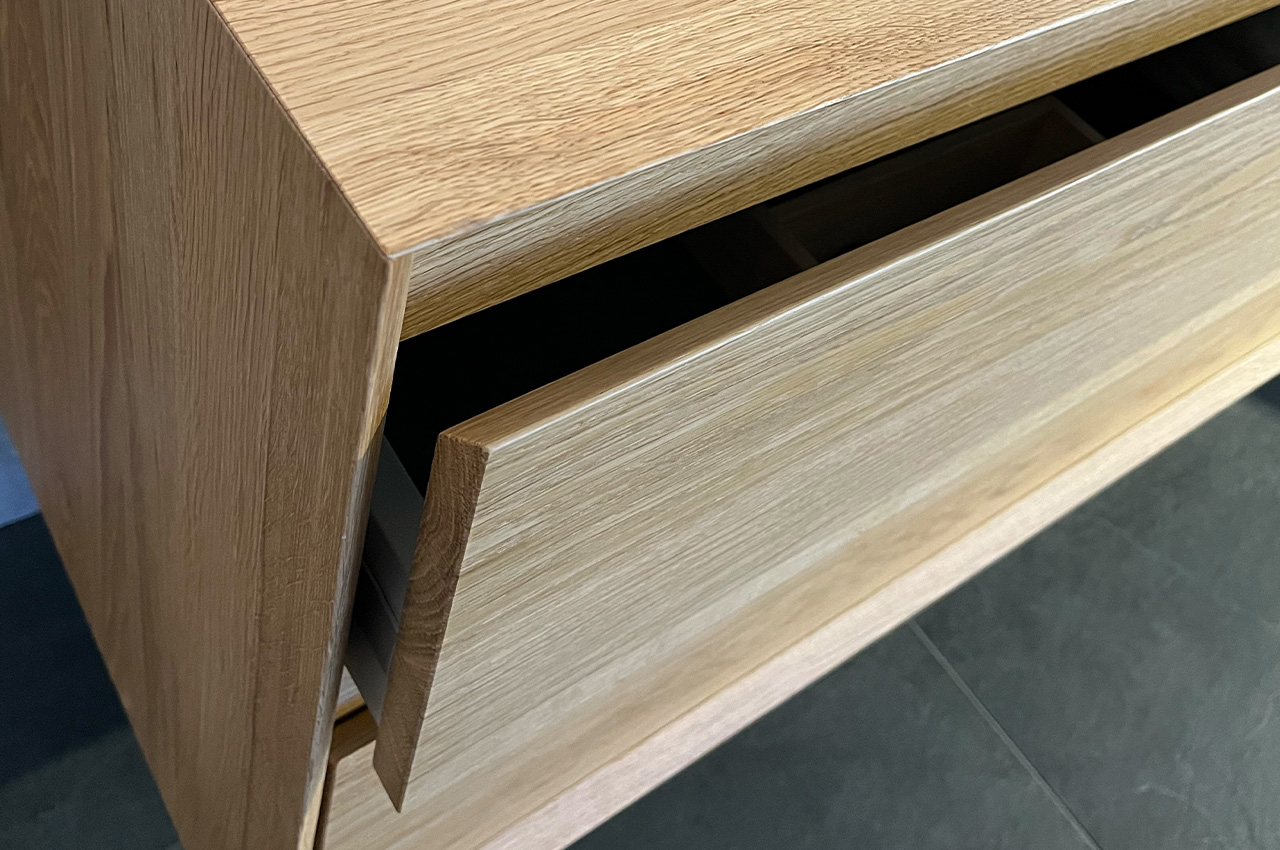 Eine Nahaufnahme eines Holzschranks, dessen eine Schublade teilweise geöffnet ist und den Blick auf die Einteiler im Inneren freigibt. Der Schrank steht auf einem dunklen Fliesenboden.