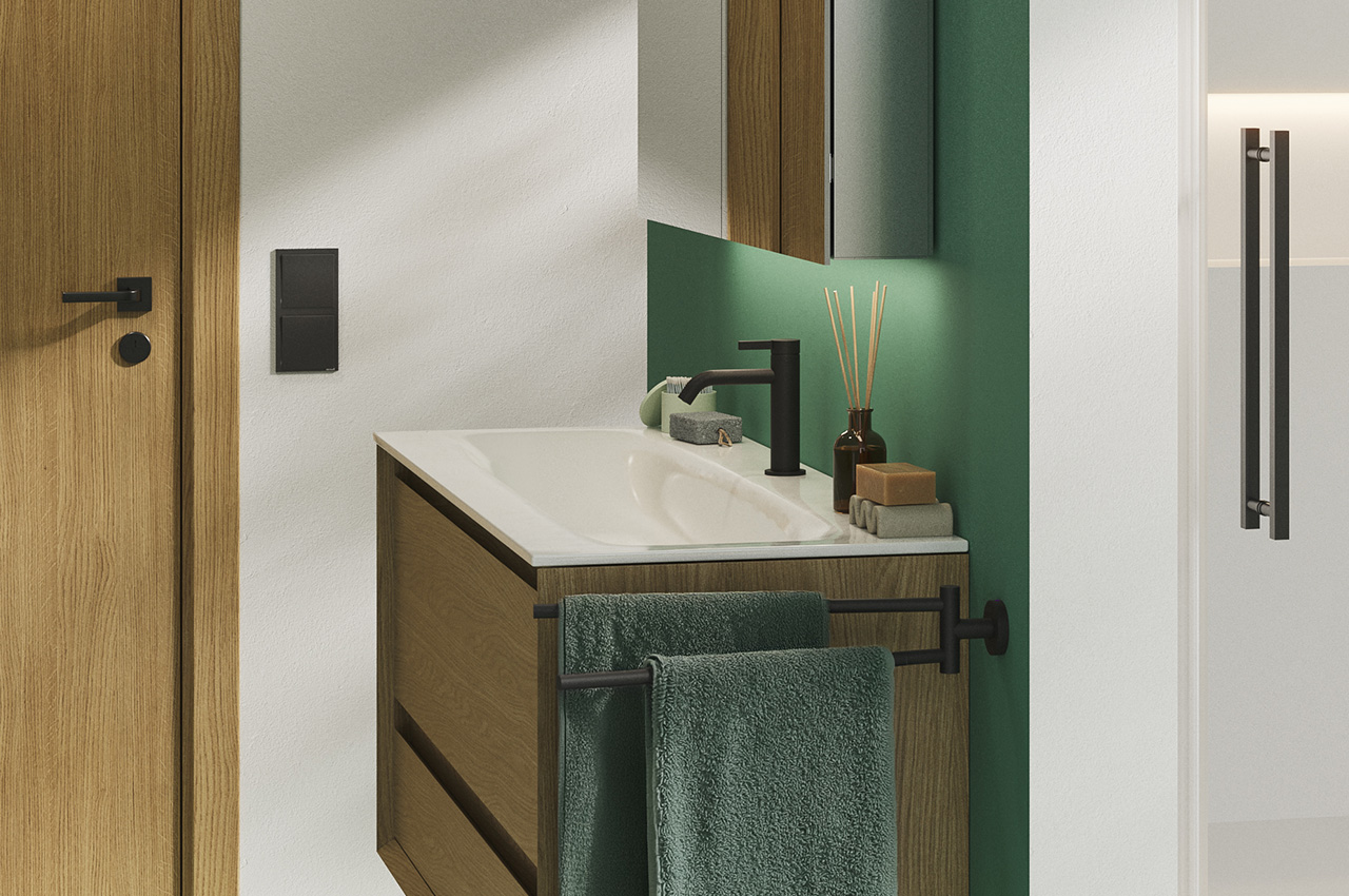 Ein modernes Badezimmer mit einem Waschtisch aus Holz, einem weißen Waschbecken, schwarzen Armaturen, grünen Handtüchern und einer grünen Akzentwand. Zu sehen sind eine Tür und ein Spiegelschrank, rechts davon eine Duschkabinentür aus Glas.