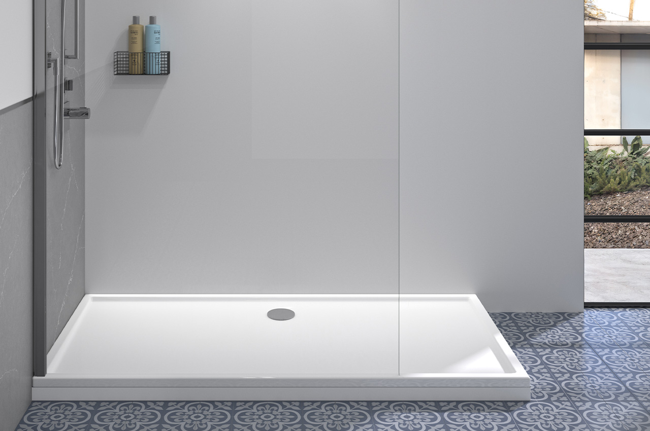 Moderne begehbare Dusche mit weißer Duschwanne, Glastrennwand, einem an der Wand befestigten Regal für Toilettenartikel und gemusterten blauen und grauen Bodenfliesen. Durch ein nahegelegenes Fenster fällt Sonnenlicht herein.